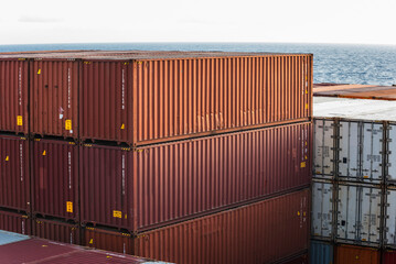 Fototapeta premium View on the top of containers loaded on deck of the large cargo ship. She is sailing through calm, blue ocean. 