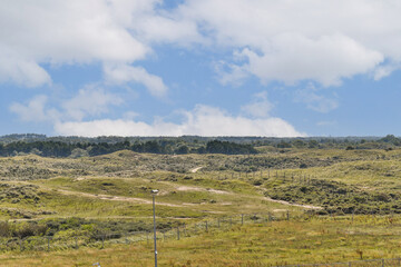 Naklejka premium A wide view of a verdant landscape under a partly cloudy sky, featuring rolling hills and a serene atmosphere, ideal for nature enthusiasts and photographers.