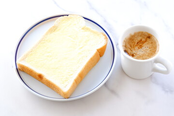 マーガリンを塗った厚切りパンと、淹れたてで香りのよいコーヒーで、朝食のイメージ
