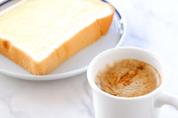 マーガリンを塗った厚切りパンと、淹れたてで香りのよいコーヒーで、朝食のイメージ
