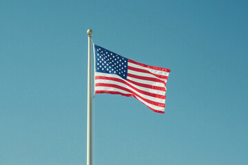 Naklejka premium American flag waving against clear blue sky, patriotic symbol of USA independence and freedom