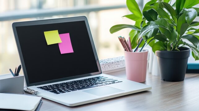 Laptop with sticky notes, pencils, and plants on a desk.