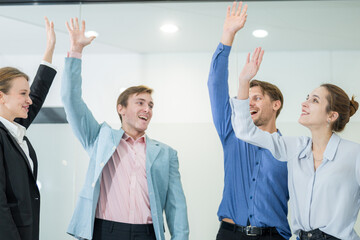 Business team celebrates success in a modern office during a morning meeting with raised hands and...