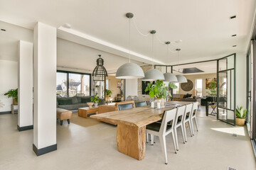 A bright and spacious open-concept living area featuring a large dining table, stylish lighting, and green plants. Ideal for contemporary living and social gatherings.