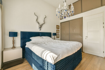 A modern bedroom featuring a blue velvet bed, a stylish chandelier, and tasteful wall decorations, creating a sophisticated and cozy atmosphere.