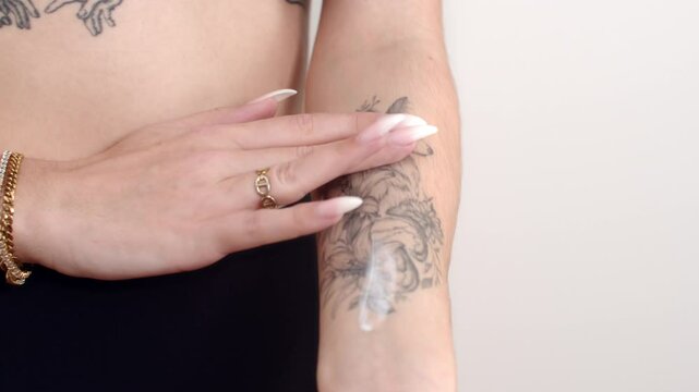 Tattooed arm being moisturized with cream using fingers in medium shot