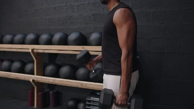 Black man lifting dumbbells in modern gym with medicine ball rack. Hammer curls in modern gym.