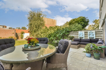 A beautifully arranged outdoor area featuring stylish seating and a glass table surrounded by lush greenery, perfect for relaxation and gatherings.
