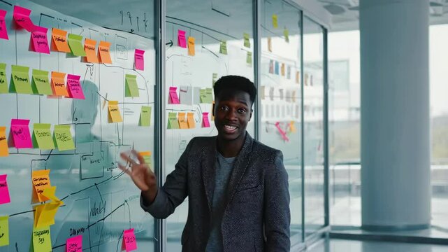 African American Employee in Office Looking at Glass Wall with Sticky Notes for Scrum Methodology