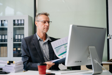 Confident businessman working on finance analysis with a tablet and laptop at office desk.
