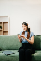 Obraz premium Asian woman using the smartphone and tablet on the sofa at home.