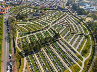 Aerial view of a large, neatly arranged cemetery with winding paths and gravestones, surrounded by...