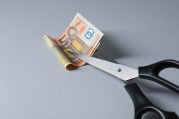Scissors with euro banknote on gray background, closeup. Space for text