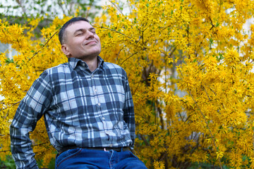 portrait of a man on the background of yellow forsythia flowers, spring nature and blossoms