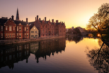 Fototapeta premium Buildings reflected in the still waters of the River Great Ouse as the sun rises in Bedford, England with the Town Bridge in the distance