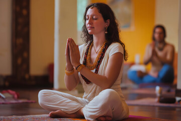 Woman practicing bhakti yoga with praying hands in lotus position, meditating with closed eyes in a yoga studio