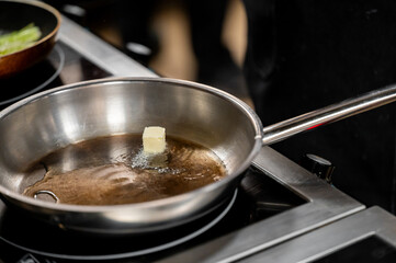 A close-up of a stainless steel skillet with a small cube of butter melting in the hot oil, capturing the essence of cooking and food preparation.