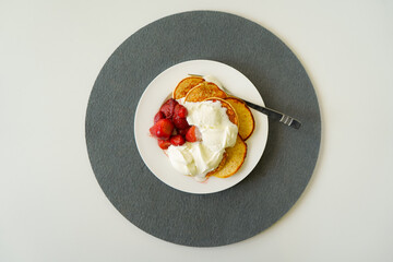 Centered pancakes with red strawberries and cream on a white plate that it on a grey felt coaster on a white table background