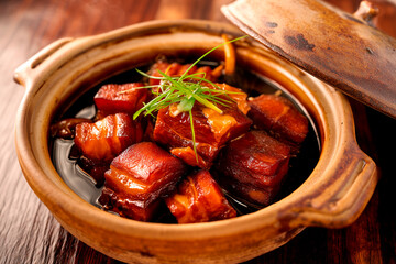 Top-down food photography of braised pork belly in a rustic clay pot, neatly arranged pork chunks with caramelized edges glistening under softbox lighting