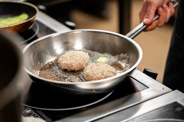 A close-up of two breaded patties frying in a stainless steel skillet, accompanied by sizzling oil, showcasing the cooking process in a professional kitchen.