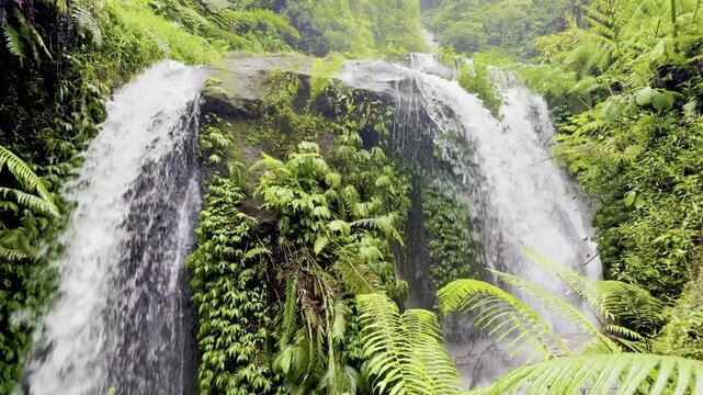 waterfall next to Banyumala Twin Waterfall flowing from a cliff surrounded by tropical dense jungle vegetation. Munduk waterfall trail, Wanagiri village. Best hikes on Bali, Indonesia