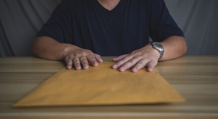 Man holding large brown envelope on table, representing confidential documents, delivery, or important business communication.