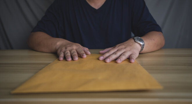 Man holding large brown envelope on table, representing confidential documents, delivery, or important business communication.