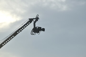 video camera hanging on heavy crane for shooting top view in sunset sky background