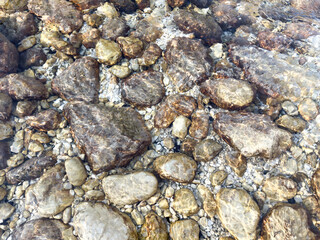 clear shallow river water flowing over assorted stones. natural pattern with sunlight reflections. minimalist and organic texture background with clean