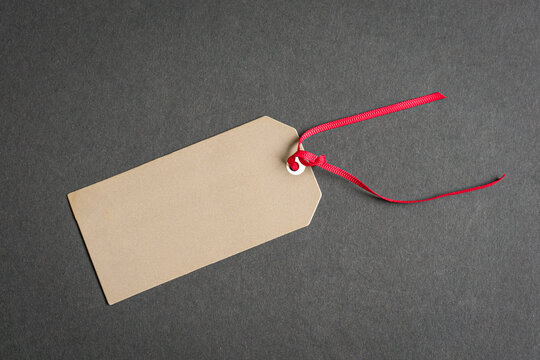 Gift tag with red ribbon on top of gray surface.