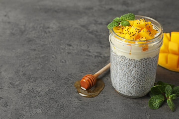 Delicious chia pudding with mango and mint in glass on gray textured table