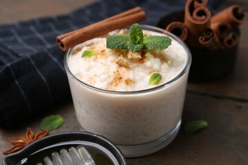 Tasty rice pudding with cinnamon, mint and nuts on wooden table, closeup