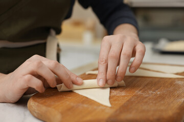 Woman rolling croissant from fresh dough at light table indoors, closeup