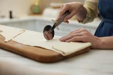 Woman cutting dough at light marble table indoors, closeup. Making croissants