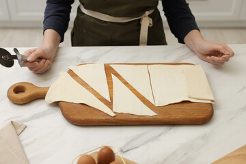 Woman with dough and cutter at light marble table indoors, closeup. Making croissants