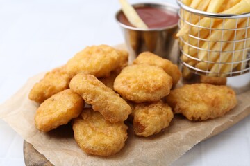 Tasty chicken nuggets, potato fries and ketchup on white tiled table, closeup