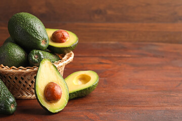 Whole and cut avocados on wooden table, closeup. Space for text