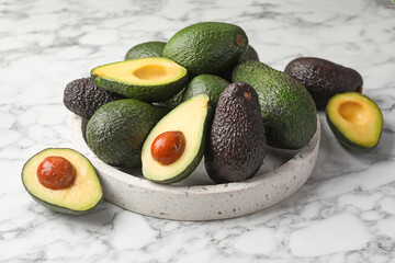 Whole and cut avocados on white marble table, closeup