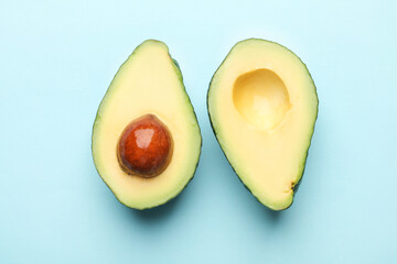 Halves of fresh avocados on light blue background, flat lay
