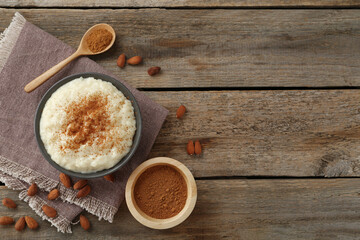 Delicious rice pudding with cinnamon and almonds on wooden table, flat lay. Space for text