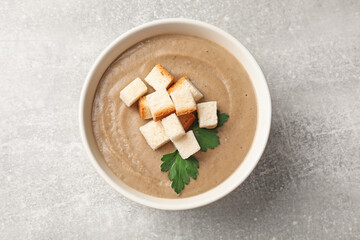 Delicious mushroom cream soup with croutons and parsley in bowl on gray textured table, top view