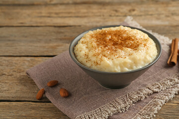 Delicious rice pudding with cinnamon and almonds on wooden table, closeup. Space for text