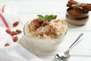 Delicious rice pudding with cinnamon, almonds and mint on white wooden table, closeup