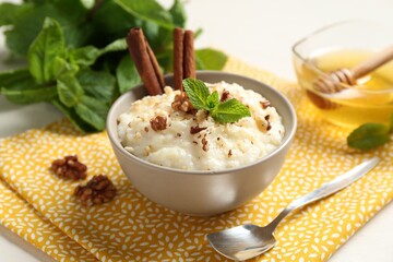 Delicious rice pudding with walnuts, cinnamon, mint and honey on white table, closeup