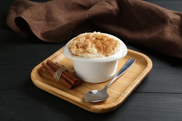 Delicious rice pudding with cinnamon in bowl and spoon on black wooden table, closeup