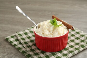 Delicious rice pudding with cinnamon, mint and spoon on wooden table, closeup