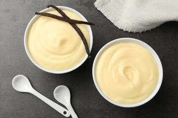 Tasty vanilla pudding with pods and spoons on black table, flat lay