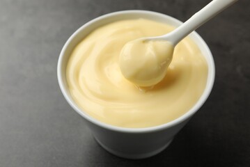 Tasty vanilla pudding with spoon on black table, closeup