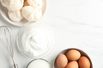 Delicious homemade meringue cookies, ingredients and whisk on white marble table, flat lay. Space...