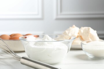 Whisk, whipped cream in bowl and other ingredients on light table, closeup. Cooking meringue cookies